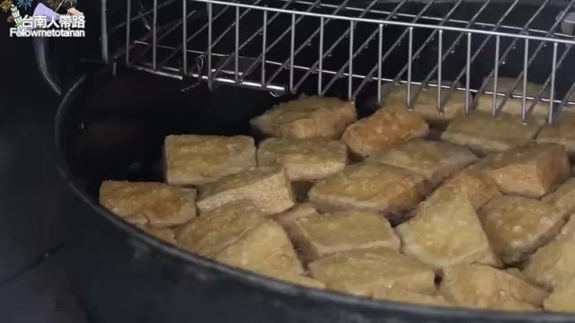 黑色平底鍋裡正在油炸的臭豆腐塊,表面呈現金黃色澤,上方架著瀝油鐵網