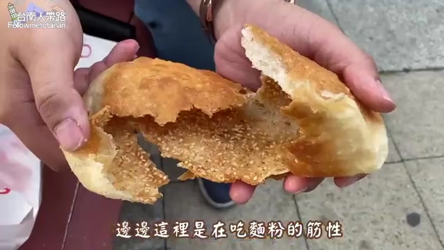 手持咬開的甜口味餅,外皮撒滿芝麻,斷面呈現層次分明的酥脆質地