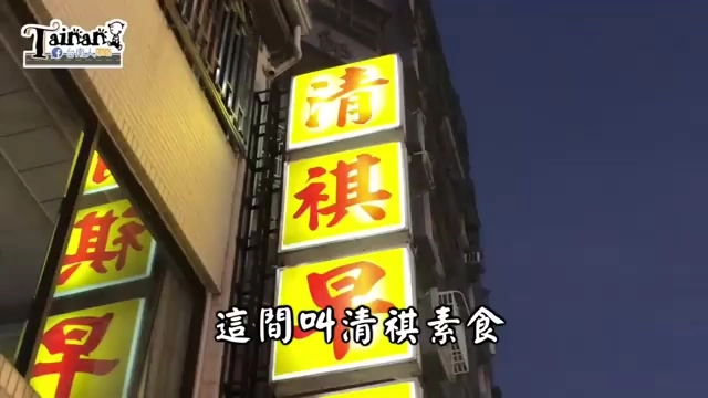 夜晚拍攝的店面外牆，黃底紅字招牌寫著「清祺」與「素食」，字幕顯示「這間叫清祺素食」
