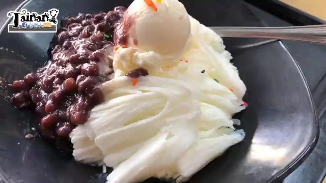黑色餐盤盛著雪花冰,鋪滿紅豆並淋上糖漿,上頭放著一球香草冰淇淋,撒上彩色米粒裝飾