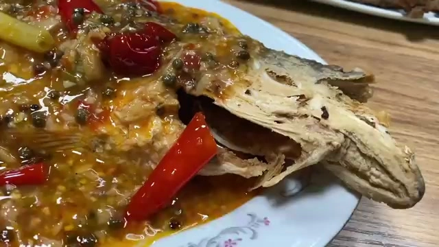 白色瓷盤盛著淋上紅色辣椒醬汁的烤魚,魚身完整可見魚頭部位,醬汁中點綴著紅椒與蒜末