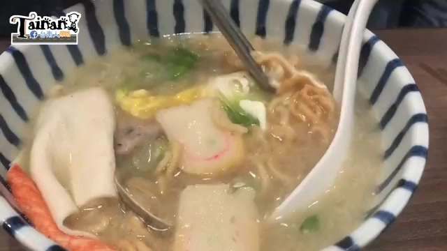 特寫鍋燒意麵，湯匙舀起麵條與配料，可見蛋皮、蔥花與其他配料交織在湯中