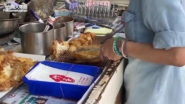 店員手拿夾子將剛炸好的蔥油餅夾出,餅皮金黃厚實,一旁擺著打包用的藍色提籃