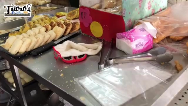 早餐店攤位鐵盤上擺滿現做饅頭與包子，一旁擺著抹布與夾子等工具