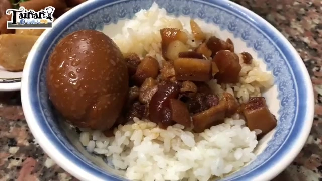 白色碗中盛著肉燥飯，淋上油亮滷汁與滷肉丁，旁邊擺著一顆完整滷蛋