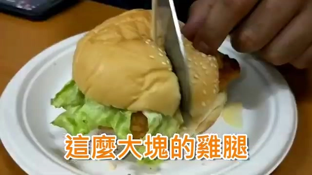 白色紙盤上的雞腿堡,刀子正切開麵包,露出生菜與炸雞腿排的斷面