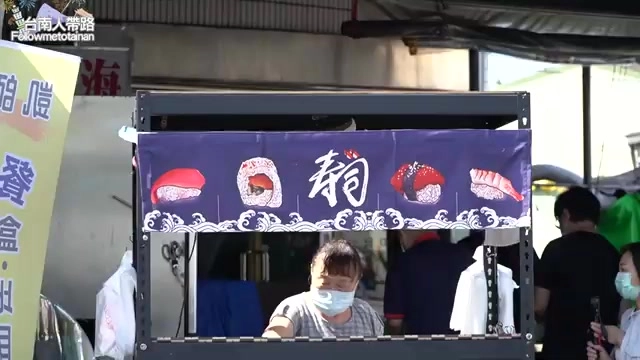 壽司攤招牌以深藍色布幔搭配握壽司插畫，師傅在攤位裡忙碌準備