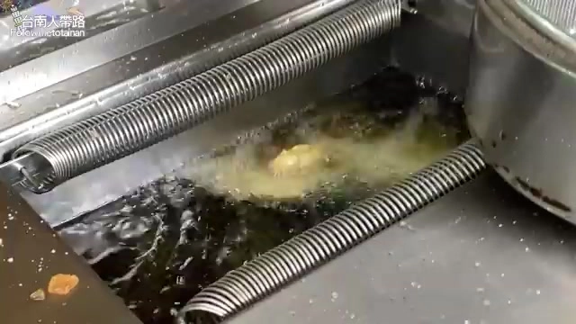 金屬油炸槽中正在油炸食物，油花翻滾冒泡