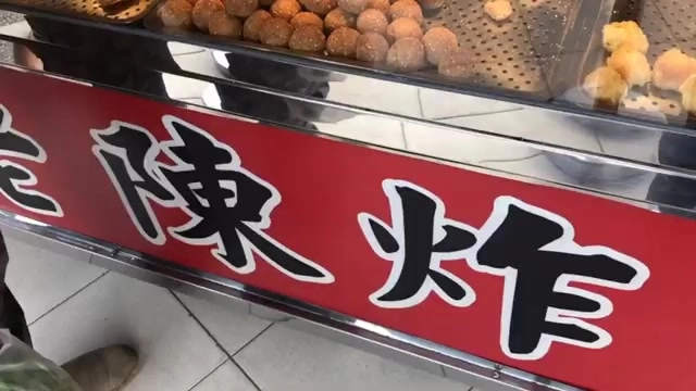 店家招牌以紅底白字寫著「陳炸」,上方展示架擺放著剛炸好的丸子與炸物