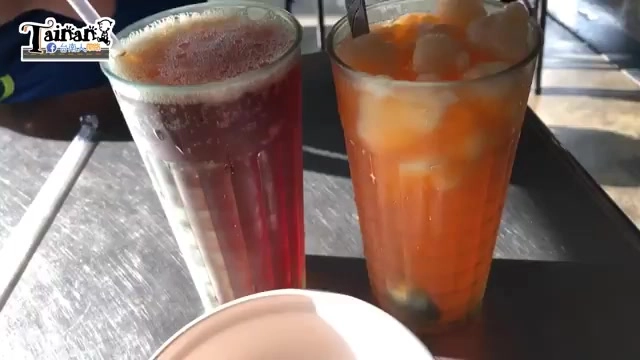 桌上擺著兩杯冷飲，左邊是深紅色紅茶，右邊是橘色的橘子水加雪奇冰，杯中冰塊清晰可見