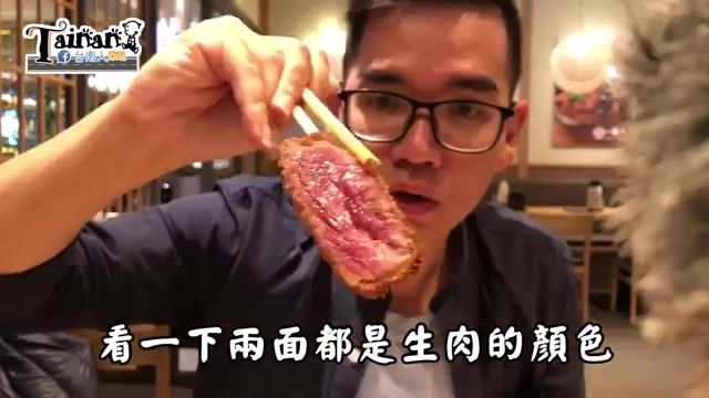 男子用筷子夾起一片生牛肉展示兩面色澤，背景可見餐廳暖色燈光