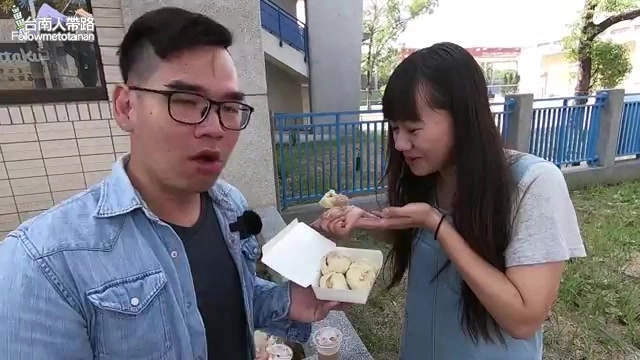 男女主持人站在戶外分享手中的小籠包,一旁擺著紙盒與飲料