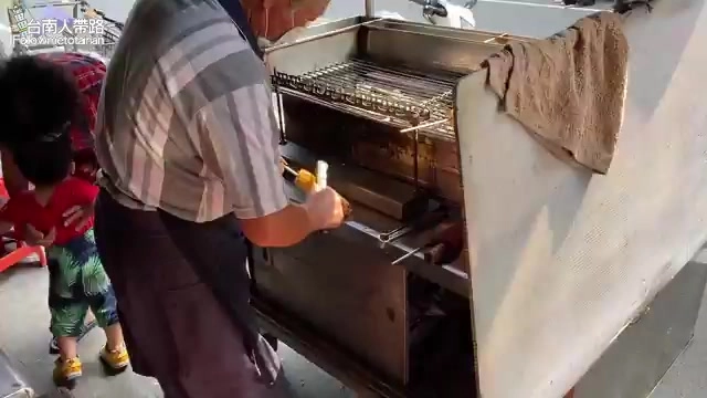 老闆站在烤爐前專注翻烤玉米,一旁孩童好奇圍觀