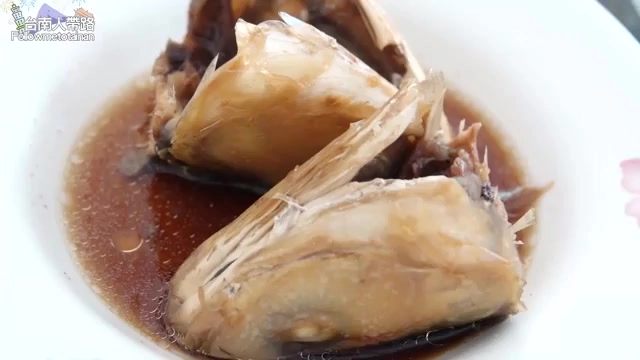 紅燒虱目魚頭盛裝在白盤中，醬汁濃郁呈深褐色，魚眼與魚骨清晰可見