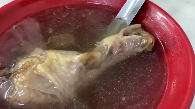 紅色碗中盛著一整隻雞腿浸泡在清澈湯汁中,湯匙置於碗邊