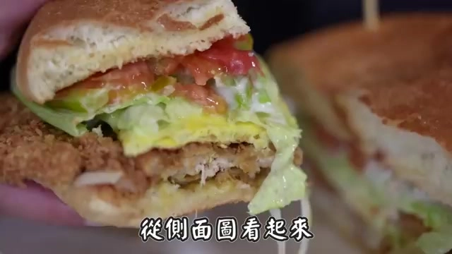 側面切開的漢堡剖面，可見厚實的番茄、生菜與炸物層層堆疊