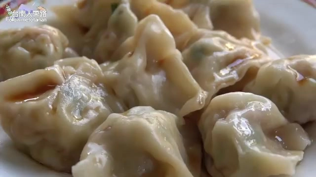 白色瓷盤中盛著多顆水餃，皮薄透亮，淋著紅油醬汁