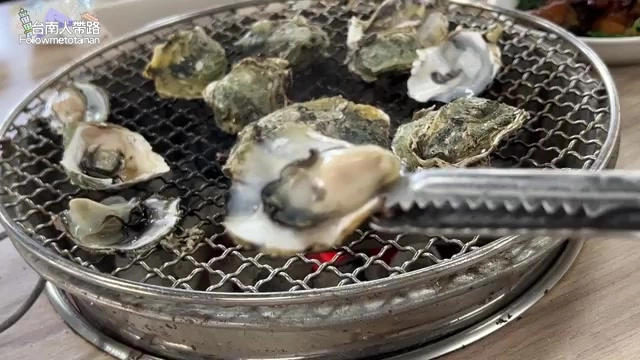 烤爐上多顆鮮蚵正在炭烤，夾子夾起一顆準備品嚐