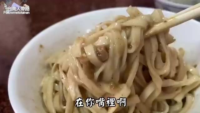 筷子挑起裹滿濃稠麻醬的寬版麵條，色澤油亮