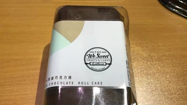 深褐色巧克力捲蛋糕包裝盒,標籤印有「THE We Sweet」品牌字樣與「巧克力捲 CHOCOLATE ROLL CAKE」中英文字樣