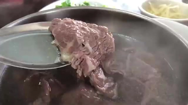 筷子夾起帶著粉紅色澤的牛肉片，浸在湯汁中緩緩熟化