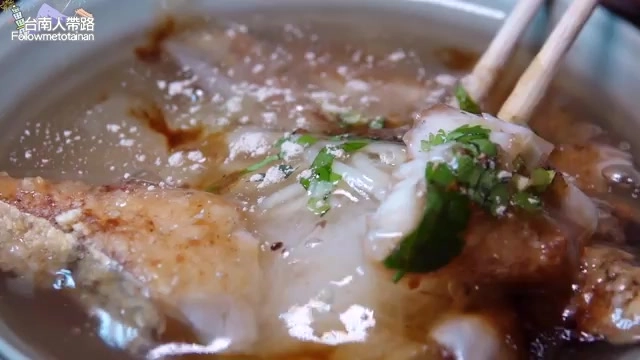 筷子夾起炸魚塊,湯裡帶著蘿蔔絲與香菜點綴,湯色清澈帶著淡淡油光