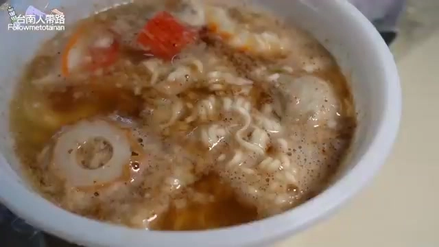 白色碗中盛著雞絲麵搭配蛋、貢丸與番茄，湯色偏紅濃郁