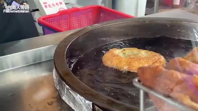 蔥肉餅正在鐵鍋上半煎炸,油光發亮,鍋邊擺著紅色籃子與其他待煎的餅