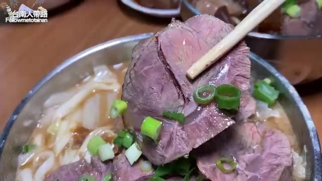 筷子夾起大塊牛肉，鋪在滿滿麵條與湯汁上，撒上翠綠蔥花